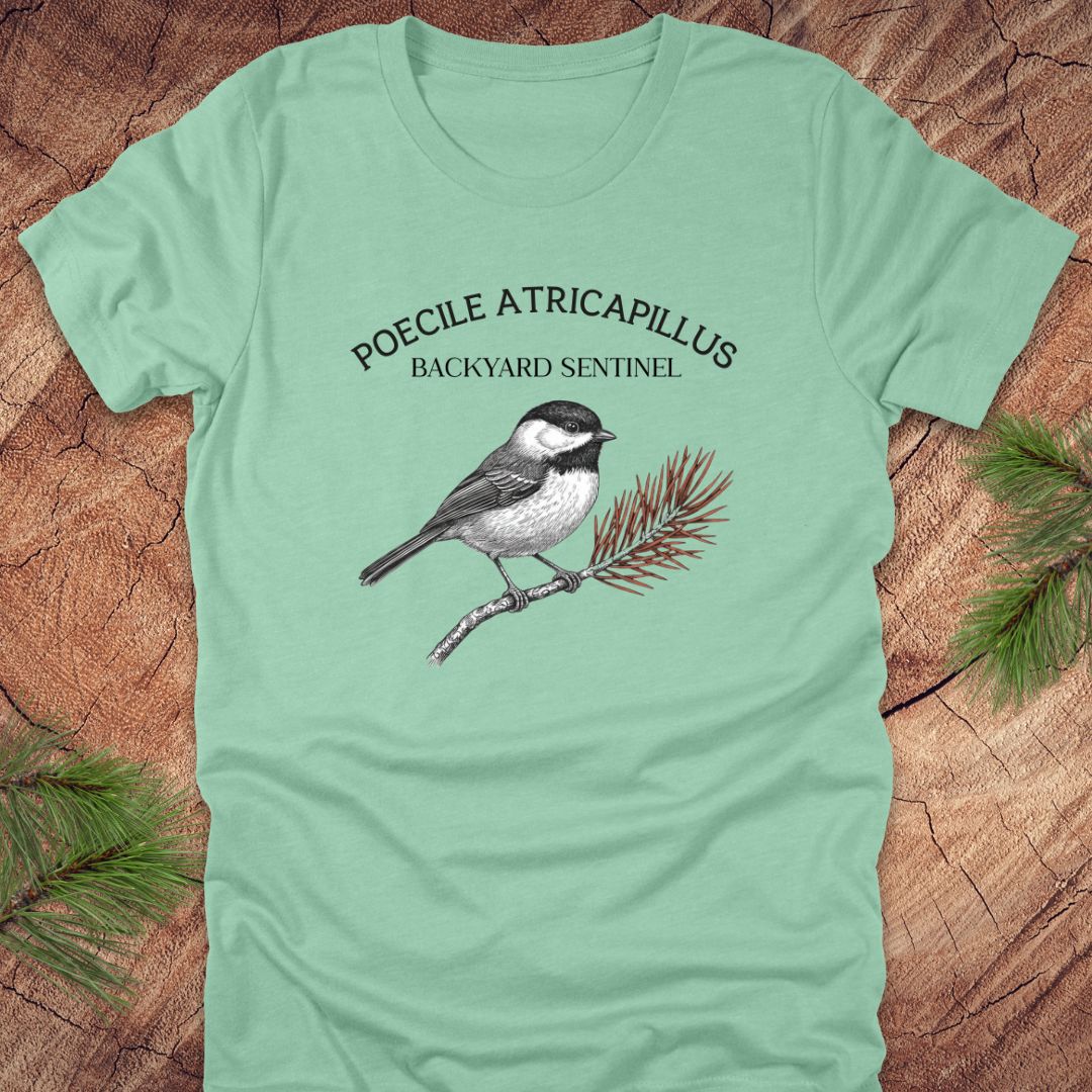Mint green t-shirt with a chickadee illustration and scientific name on a wooden surface