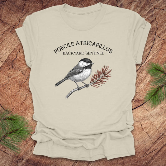 Natural t-shirt with a chickadee illustration and scientific name on a wooden surface