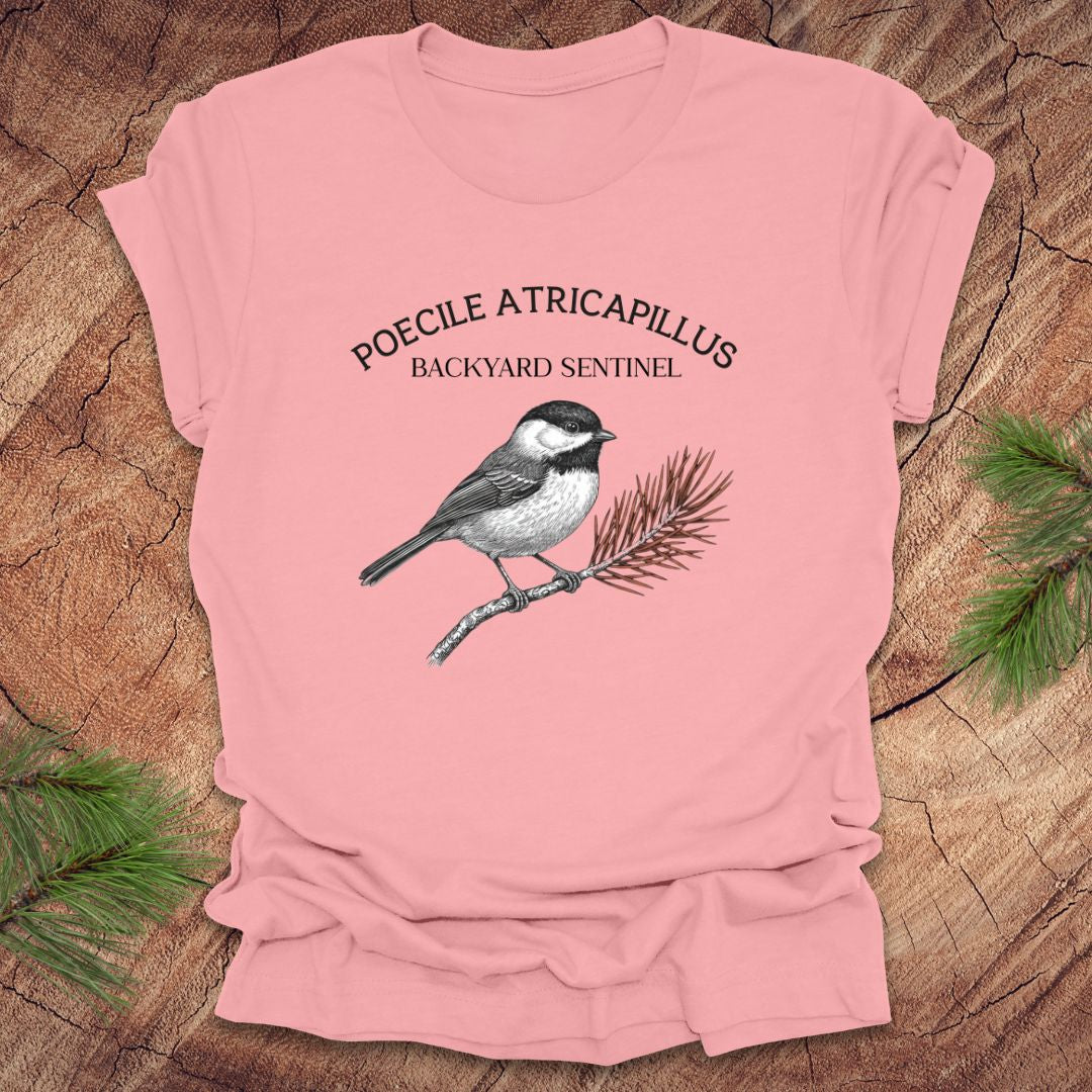 Pink t-shirt with a chickadee illustration and scientific name on a wooden surface
