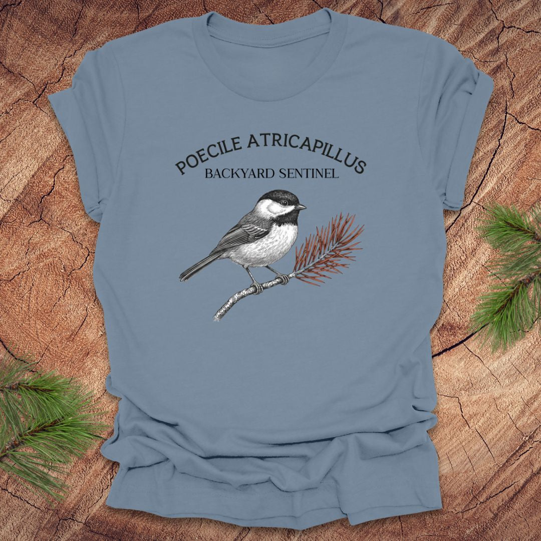 Steel blue t-shirt with a chickadee illustration and scientific name on a wooden surface