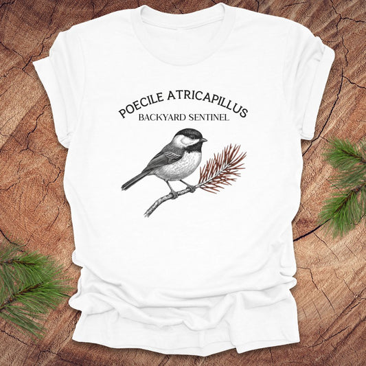 White t-shirt with a chickadee illustration and scientific name on a wooden surface