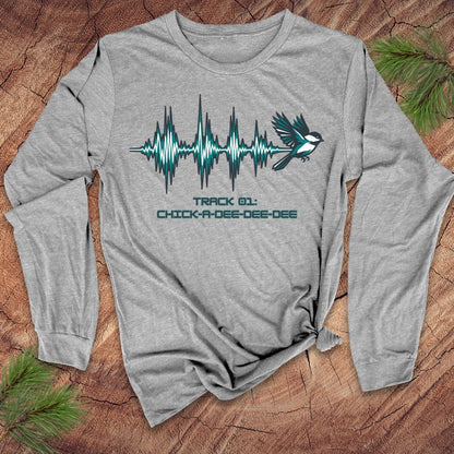 Gray long-sleeve shirt with a chickadee and sound wave design on a wooden surface