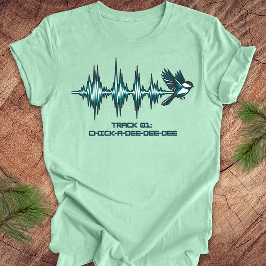 Mint green t-shirt with a chickadee and sound wave design on a wooden surface