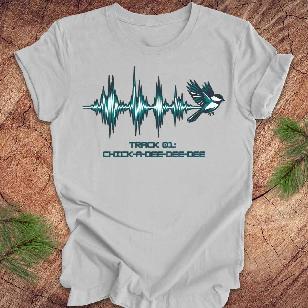 Silver t-shirt with a chickadee and sound wave design on a wooden surface