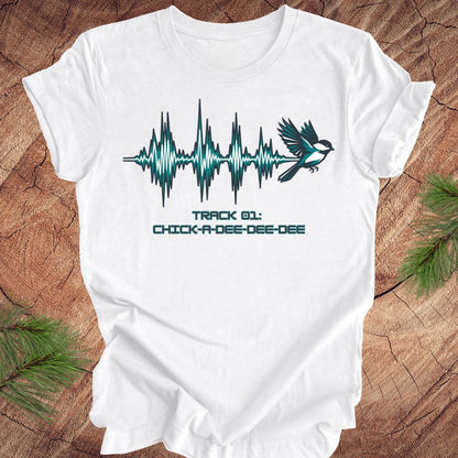 White t-shirt with a chickadee and sound wave design on a wooden surface