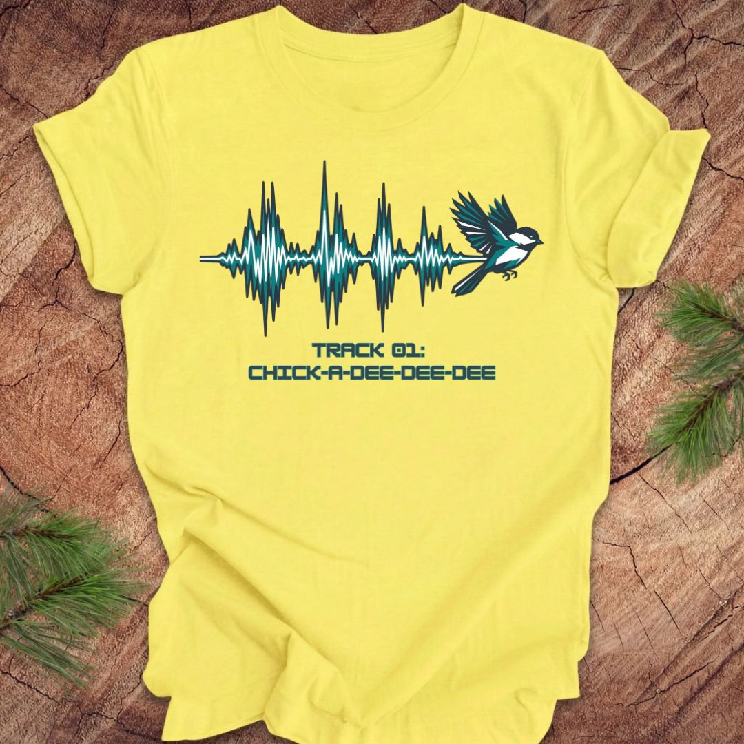 Yellow t-shirt with a chickadee and sound wave design on a wooden surface