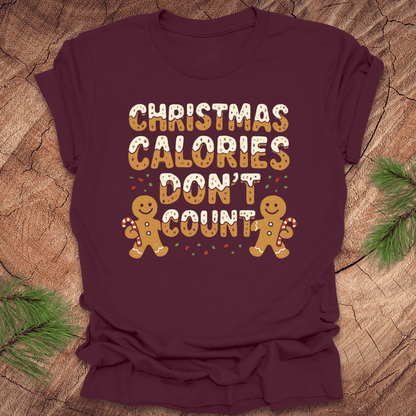 Maroon tshirt with festive gingerbread text, 'Christmas calories don't count' with gingerbread men on a wooden background.