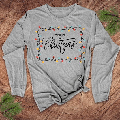 Gray long-sleeve shirt with 'Merry Christmas' design on a wooden surface with pine branches.