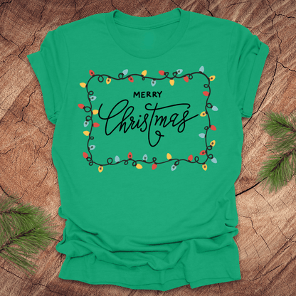 Green t-shirt with christmas lights graphic and 'Merry Christmas' design on a wooden surface