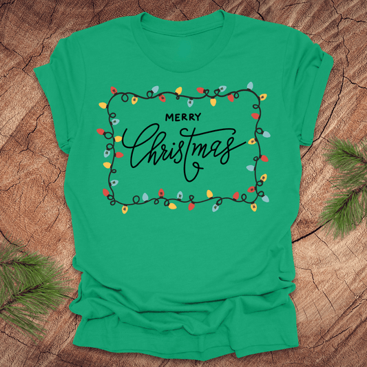 Green t-shirt with christmas lights graphic and 'Merry Christmas' design on a wooden surface