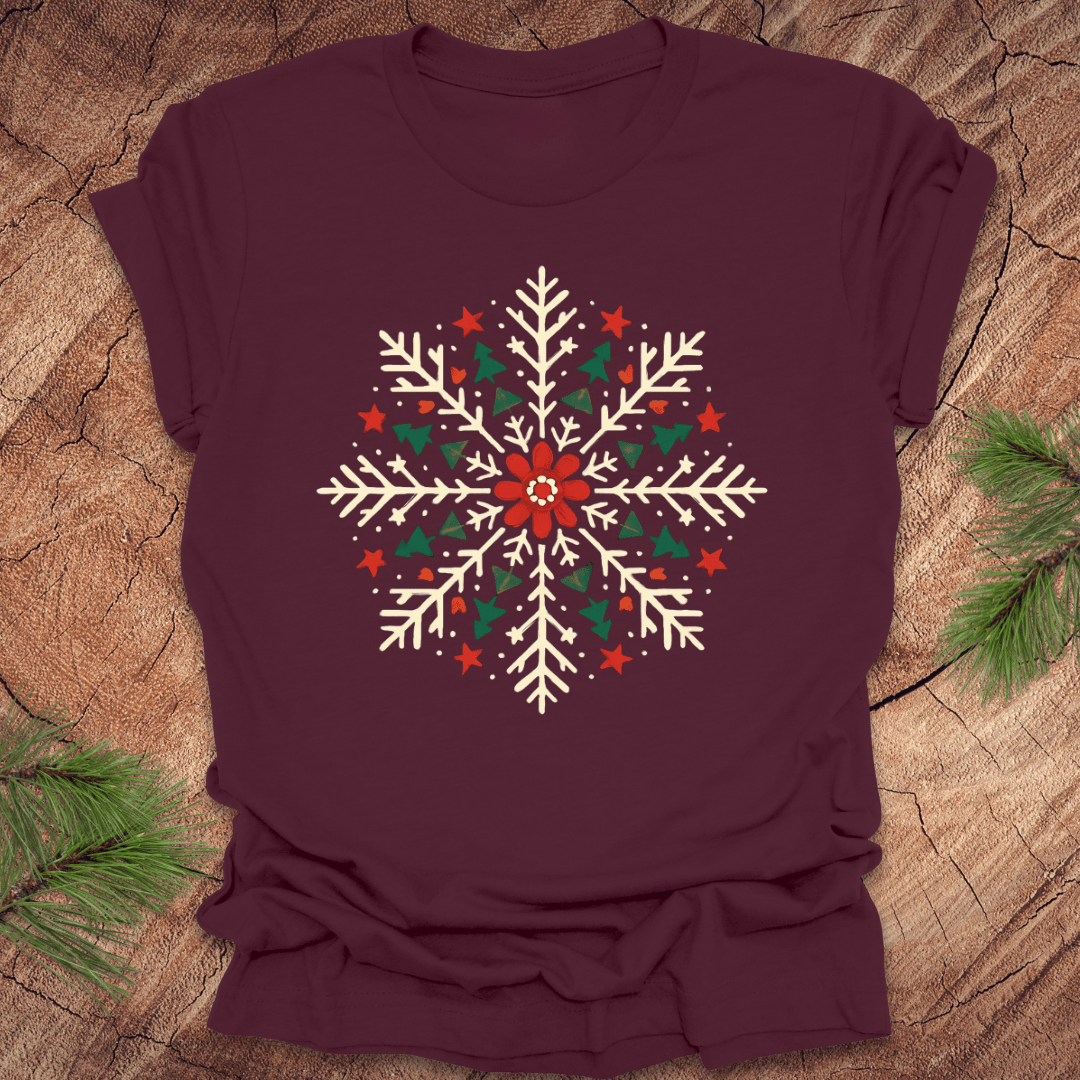 Maroon t-shirt with a colorful snowflake design on a wooden surface with pine branches.