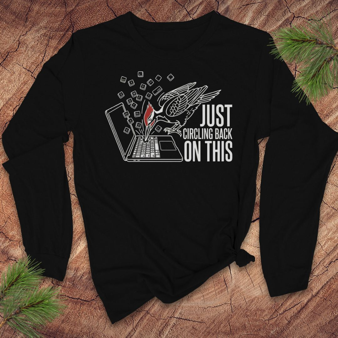 Black long-sleeve shirt with woodpecker graphic design and text on a wooden surface