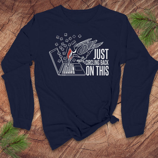 Navy blue long-sleeve tshirt with woodpecker graphic design and text on a wooden surface with greenery.