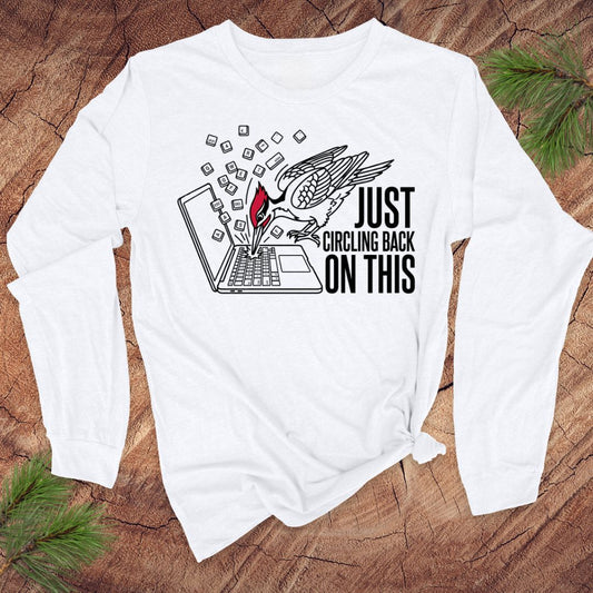 White long-sleeve shirt with woodpecker graphic design and text on a wooden surface