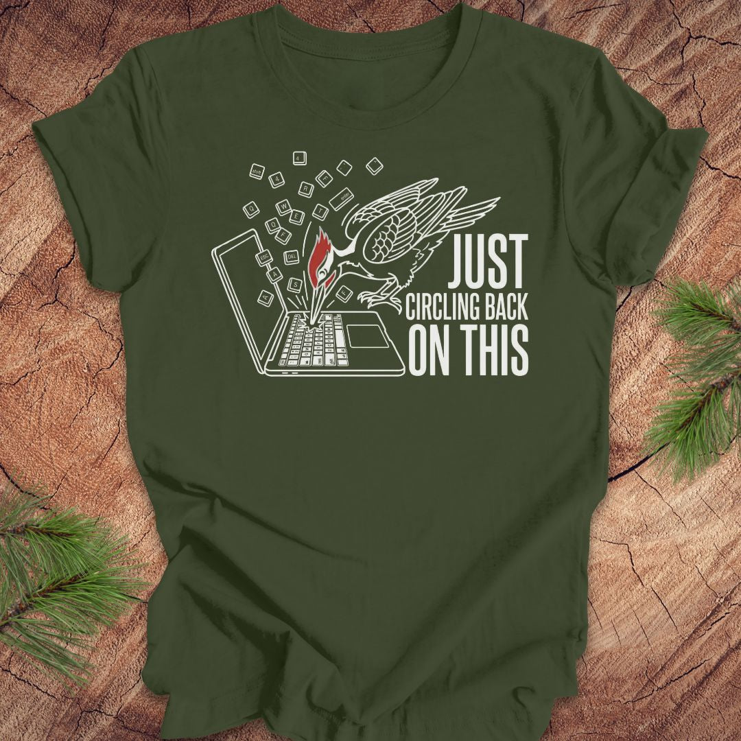 Green t-shirt with a woodpecker graphic design and text on a wooden surface