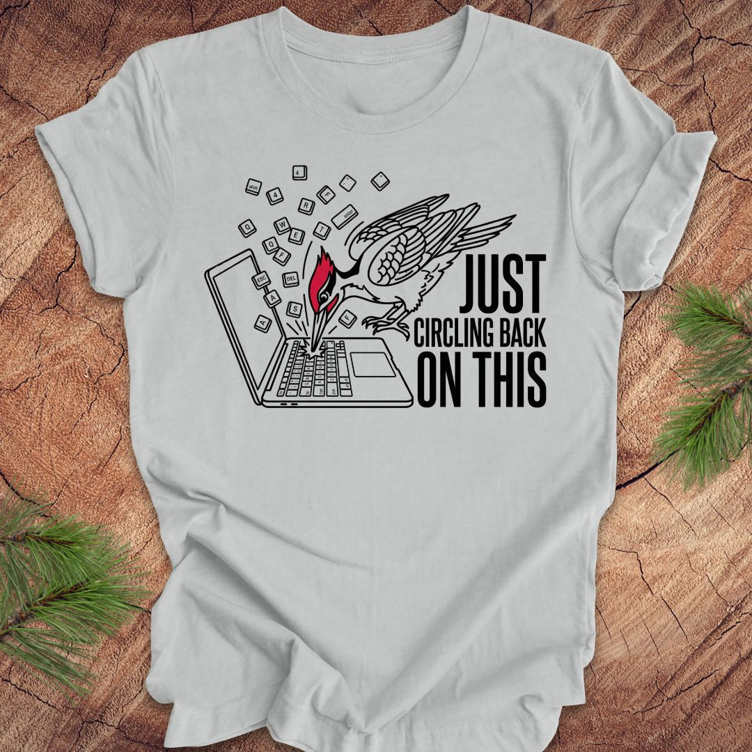 Gray t-shirt with graphic woodpecker design and text on a wooden surface