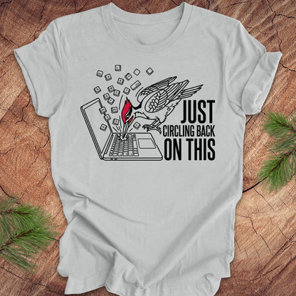 Gray t-shirt with graphic woodpecker design and text on a wooden surface