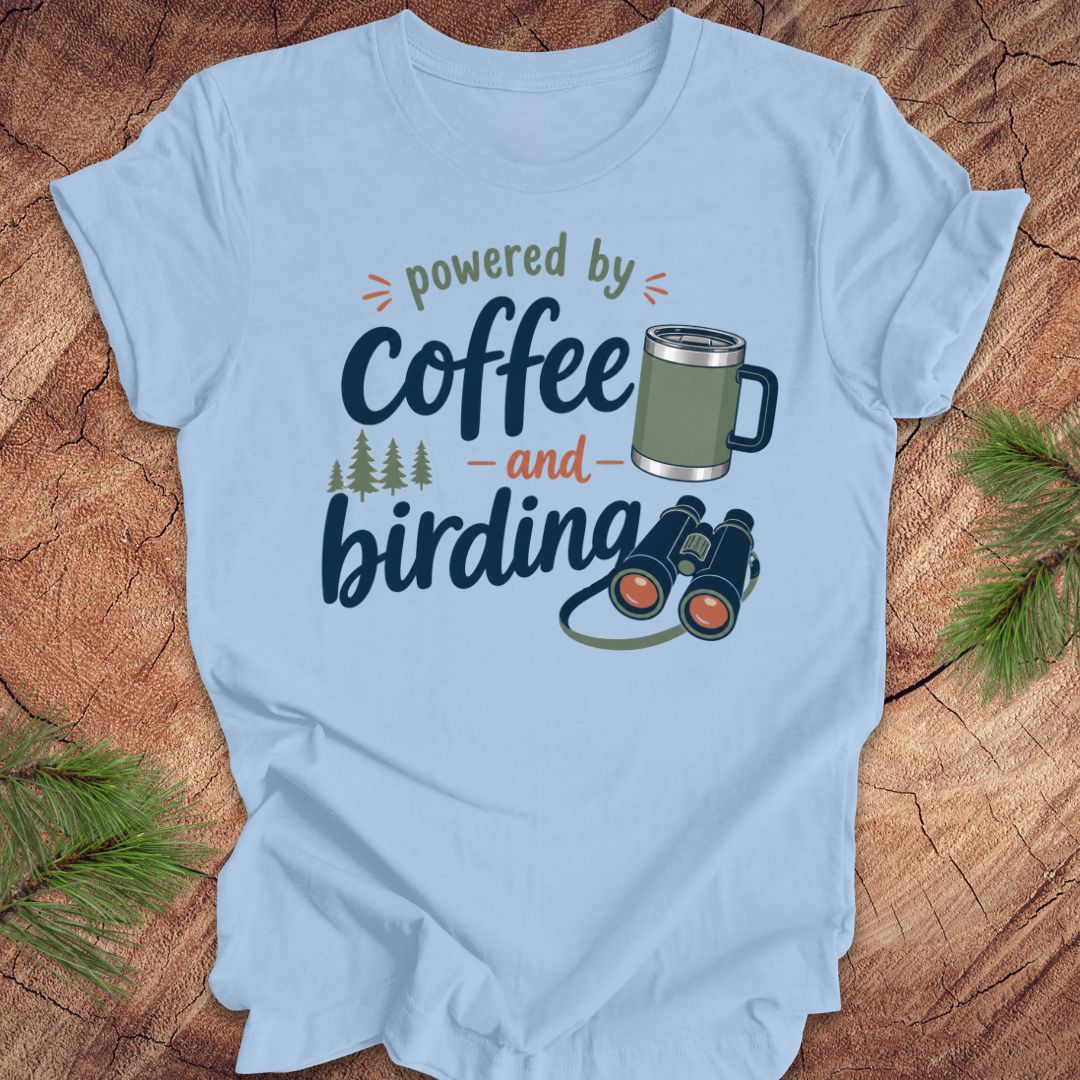 Light blue t-shirt with 'powered by coffee and birding' design on a wooden surface.