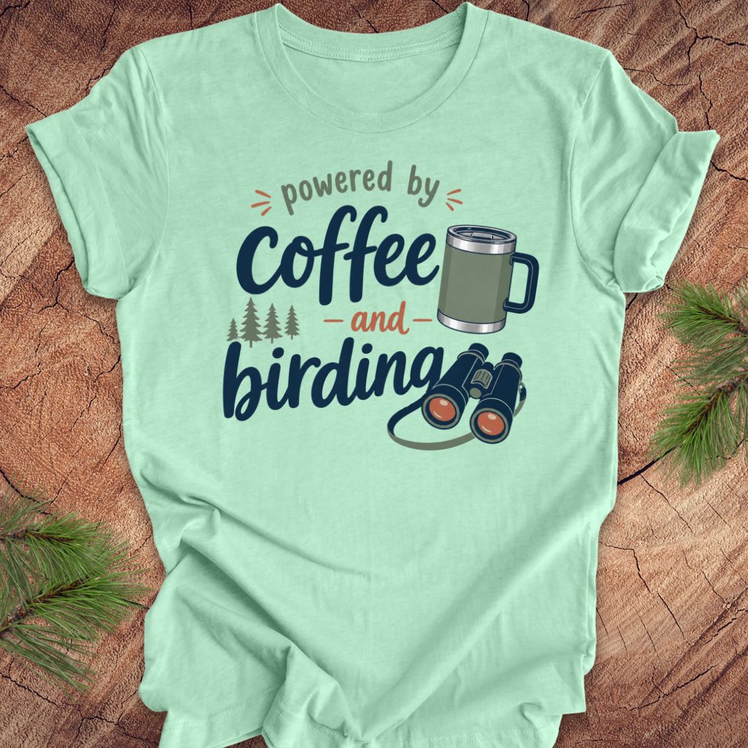 Mint green t-shirt with 'powered by coffee and birding' design on a wooden surface.