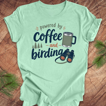 Mint green t-shirt with 'powered by coffee and birding' design on a wooden surface.