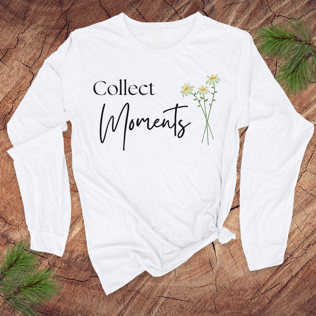 White long-sleeve tshirt with 'Collect Moments' text and daisy flowers on a wooden surface