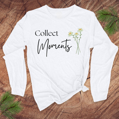 White long-sleeve tshirt with 'Collect Moments' text and daisy flowers on a wooden surface