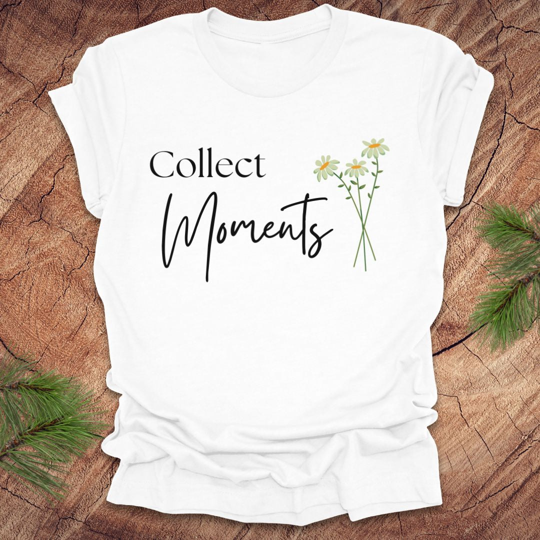 White t-shirt with 'Collect Moments' text and floral design on a wooden surface