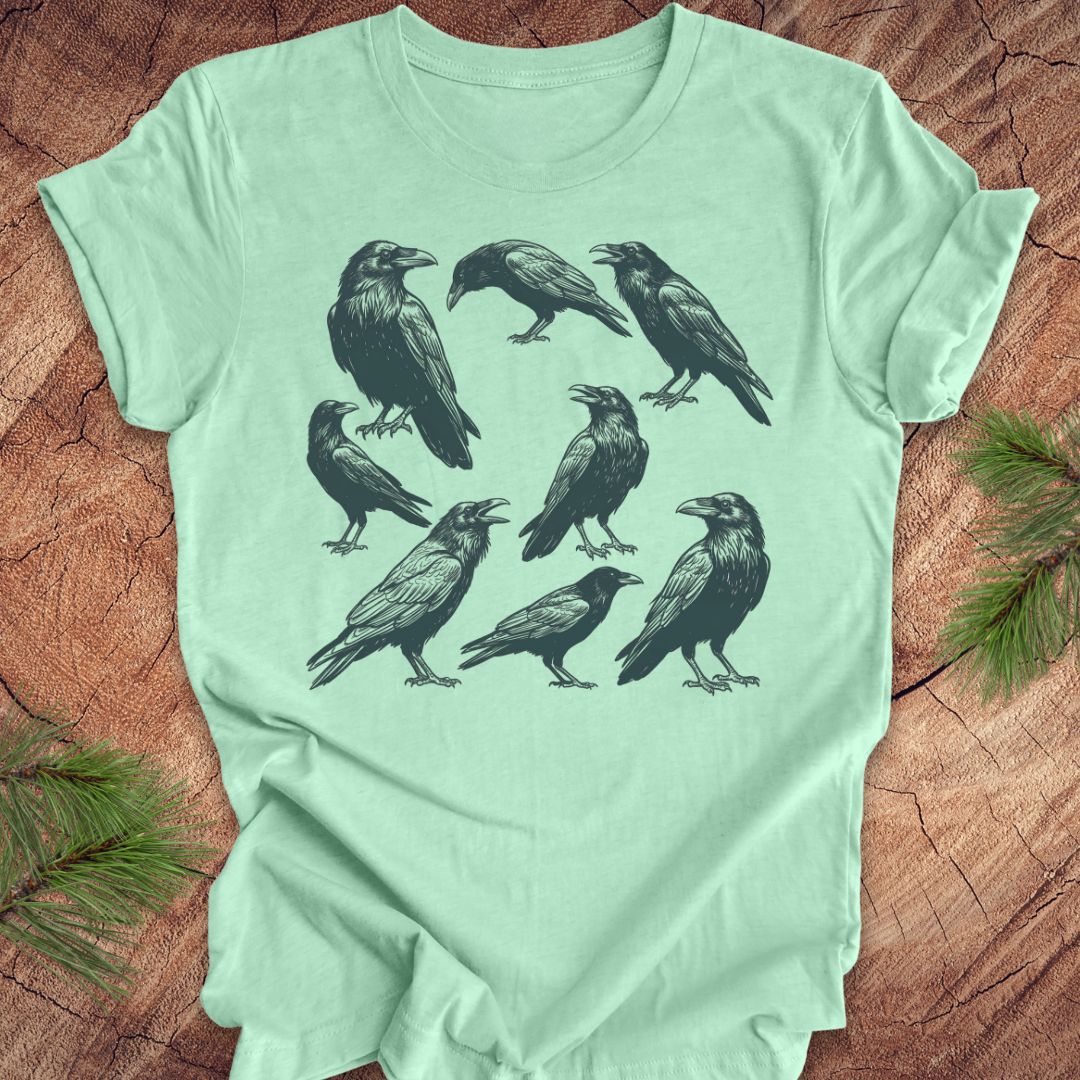 Mint green t-shirt with black crow and raven illustrations on a wooden surface