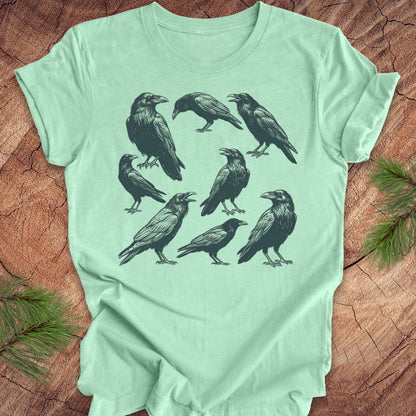 Mint green t-shirt with black crow and raven illustrations on a wooden surface