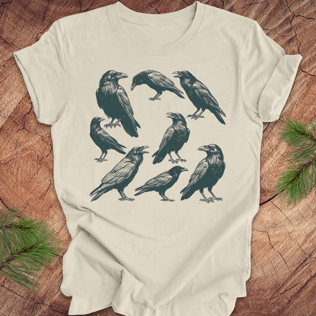 Beige t-shirt with black crow and raven illustrations on a wooden surface
