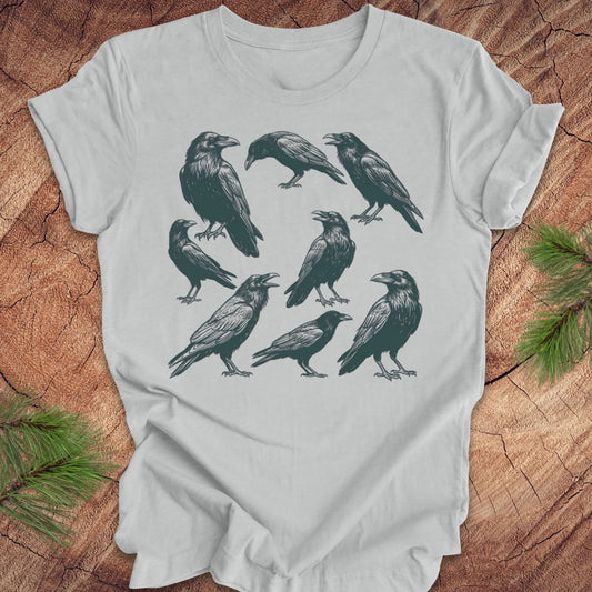 Gray t-shirt with black crow and raven illustrations on a wooden surface
