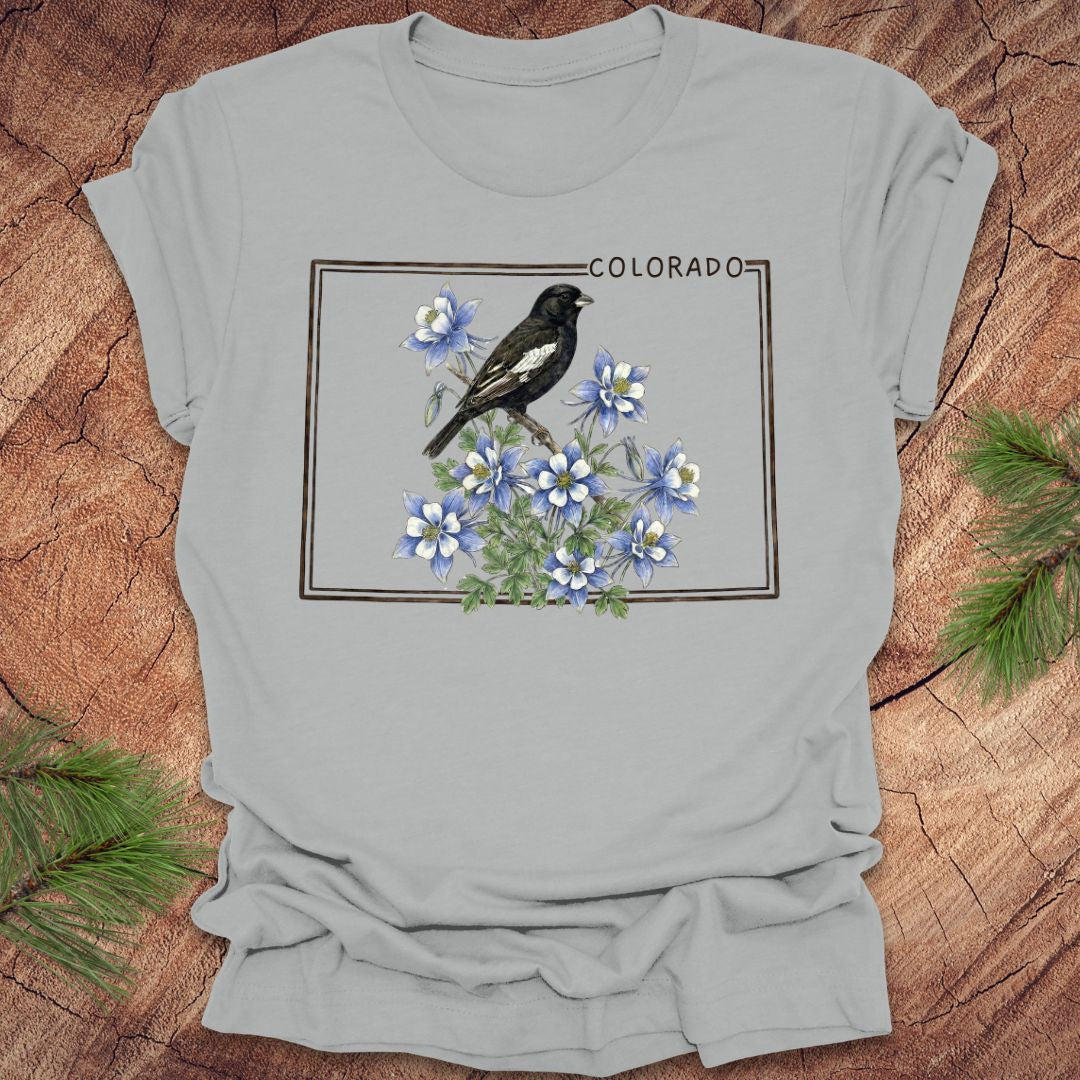 Gray t-shirt with the outline of colorado with lark bunting and columbine design on a wooden surface