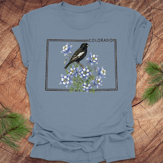 Steel blue t-shirt with the outline of colorado with lark bunting and columbine design on a wooden surface