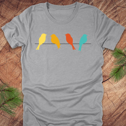 Gray t-shirt with colorful birds on a wire design on a wooden surface