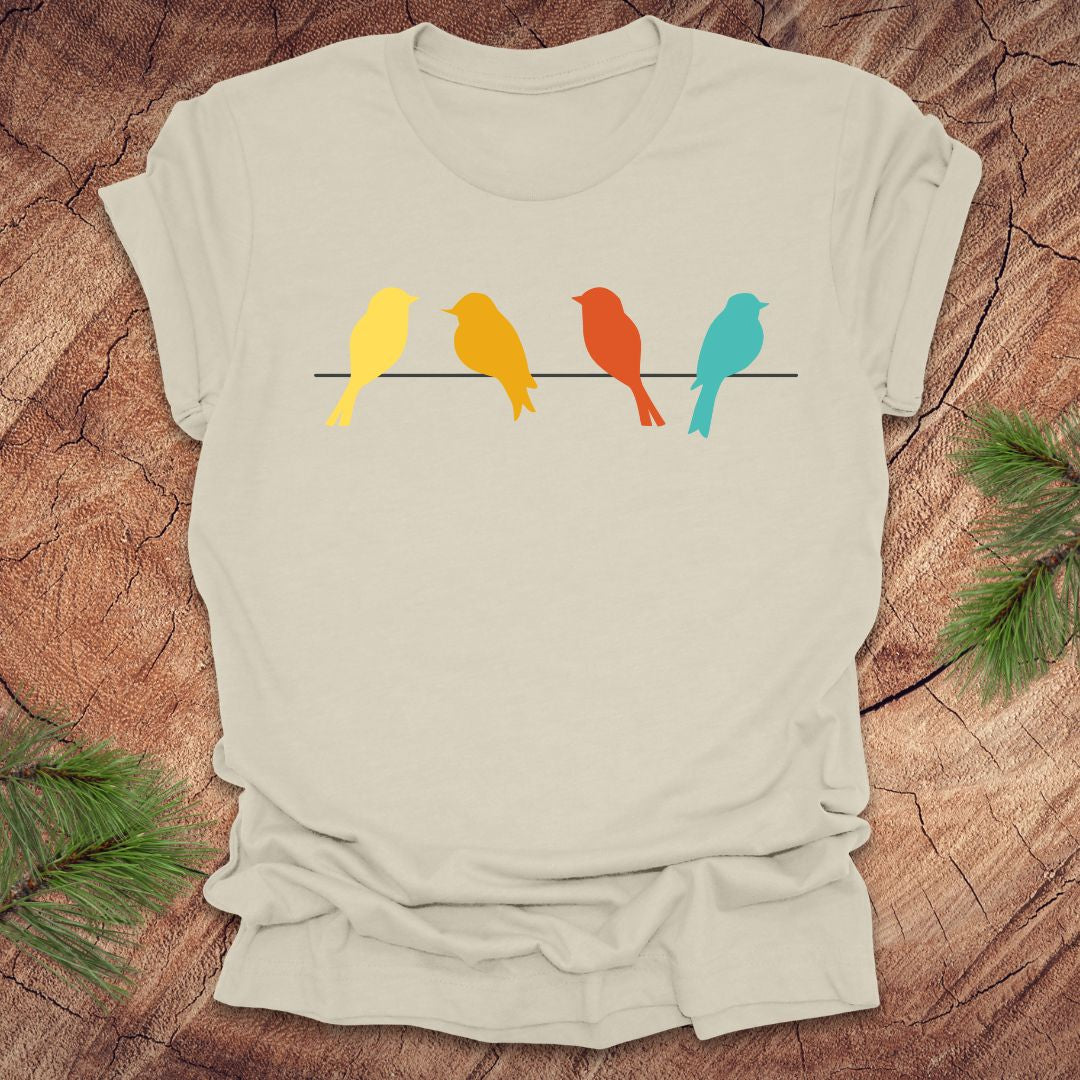 Beige t-shirt with colorful birds on a wire design on a wooden surface