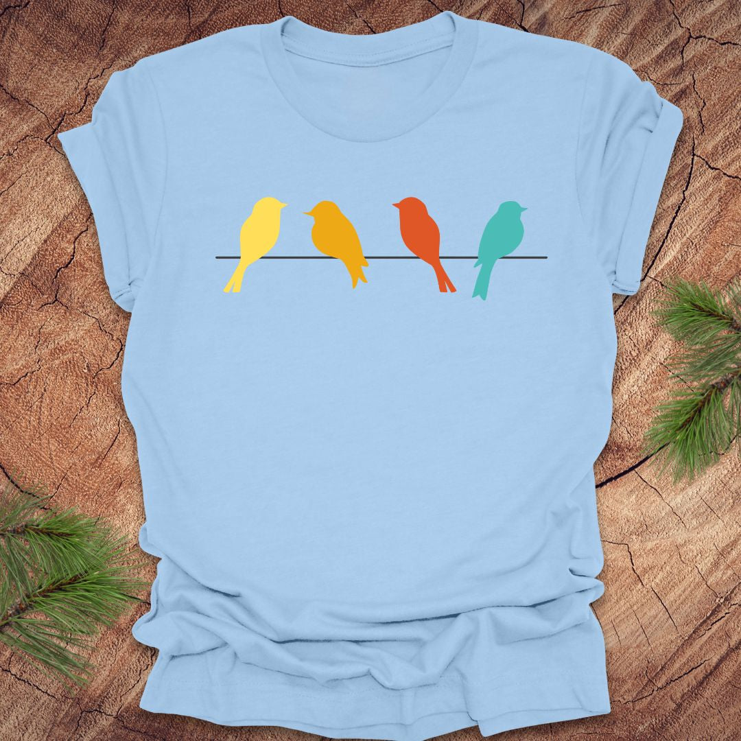 Light blue t-shirt with colorful birds on a wire design on a wooden surface