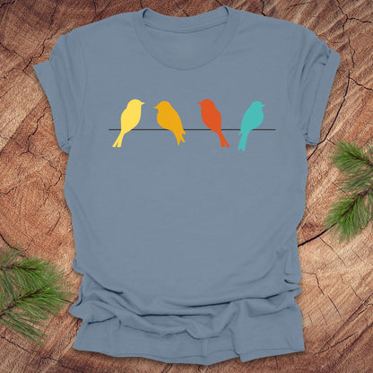 Blue t-shirt with colorful birds on a wire design on a wooden surface