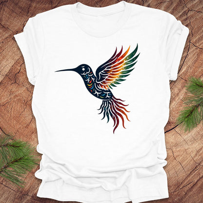 White t-shirt with a colorful hummingbird design on a wooden surface with green leaves.