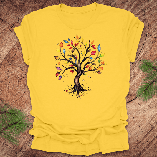 Yellow tshirt with a colorful tree design on a wood background with pine leaves.