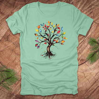 Mint green tshirt with a colorful tree design on a wood background with pine leaves.