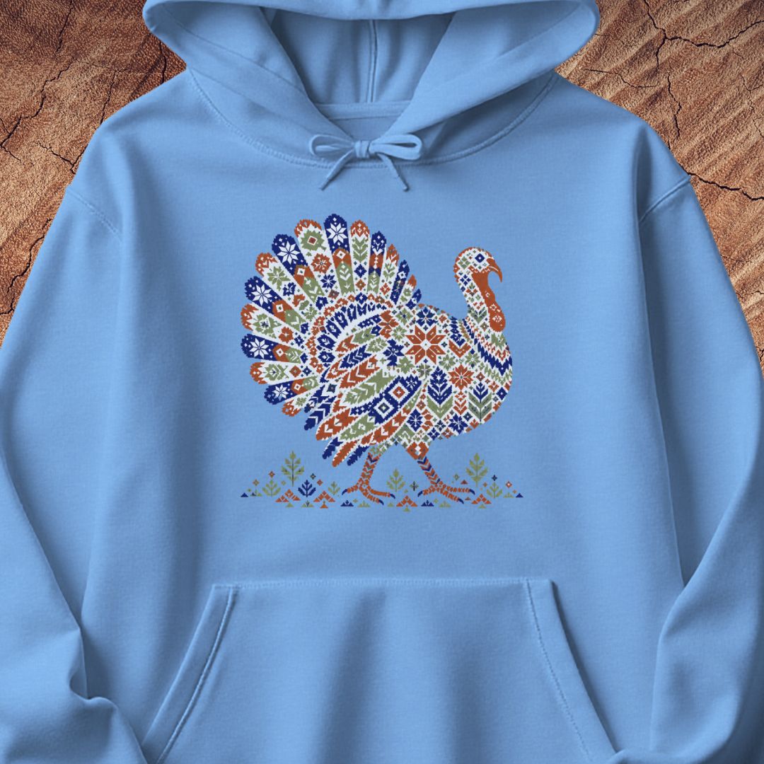 Carolina blue hoodie with a wild turkey patterned like a colorful knit sweater with snowflakes, stars, and tiny pine trees, laid flat on a rustic wood background.