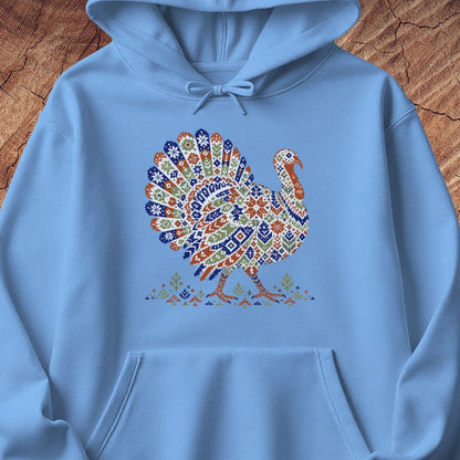 Carolina blue hoodie with a wild turkey patterned like a colorful knit sweater with snowflakes, stars, and tiny pine trees, laid flat on a rustic wood background.