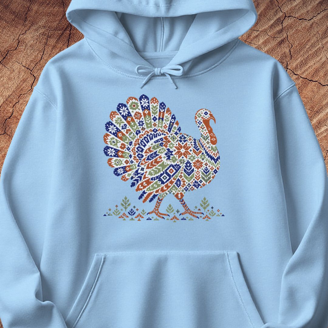 Light blue hoodie with a wild turkey patterned like a colorful knit sweater with snowflakes, stars, and tiny pine trees, laid flat on a rustic wood background.