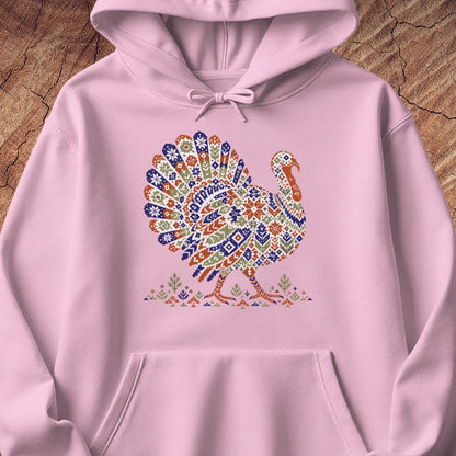 Light pink hoodie with a wild turkey patterned like a colorful knit sweater with snowflakes, stars, and tiny pine trees, laid flat on a rustic wood background.