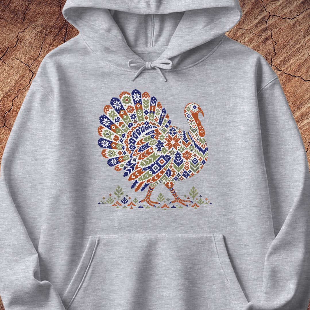 Sport grey hoodie with a wild turkey patterned like a colorful knit sweater with snowflakes, stars, and tiny pine trees, laid flat on a rustic wood background.