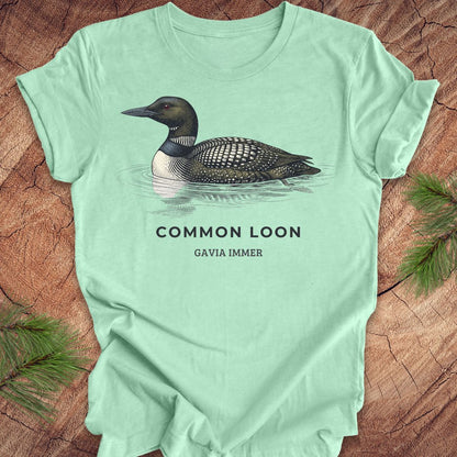 Mint green t-shirt with a common loon on a wood background.