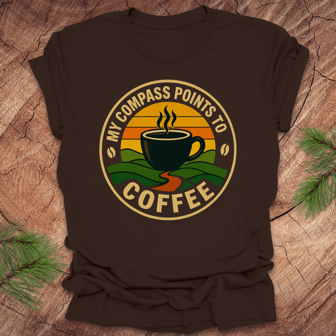 Brown t-shirt with a coffee-themed graphic and text, 'my compass points to coffee' on a wooden surface