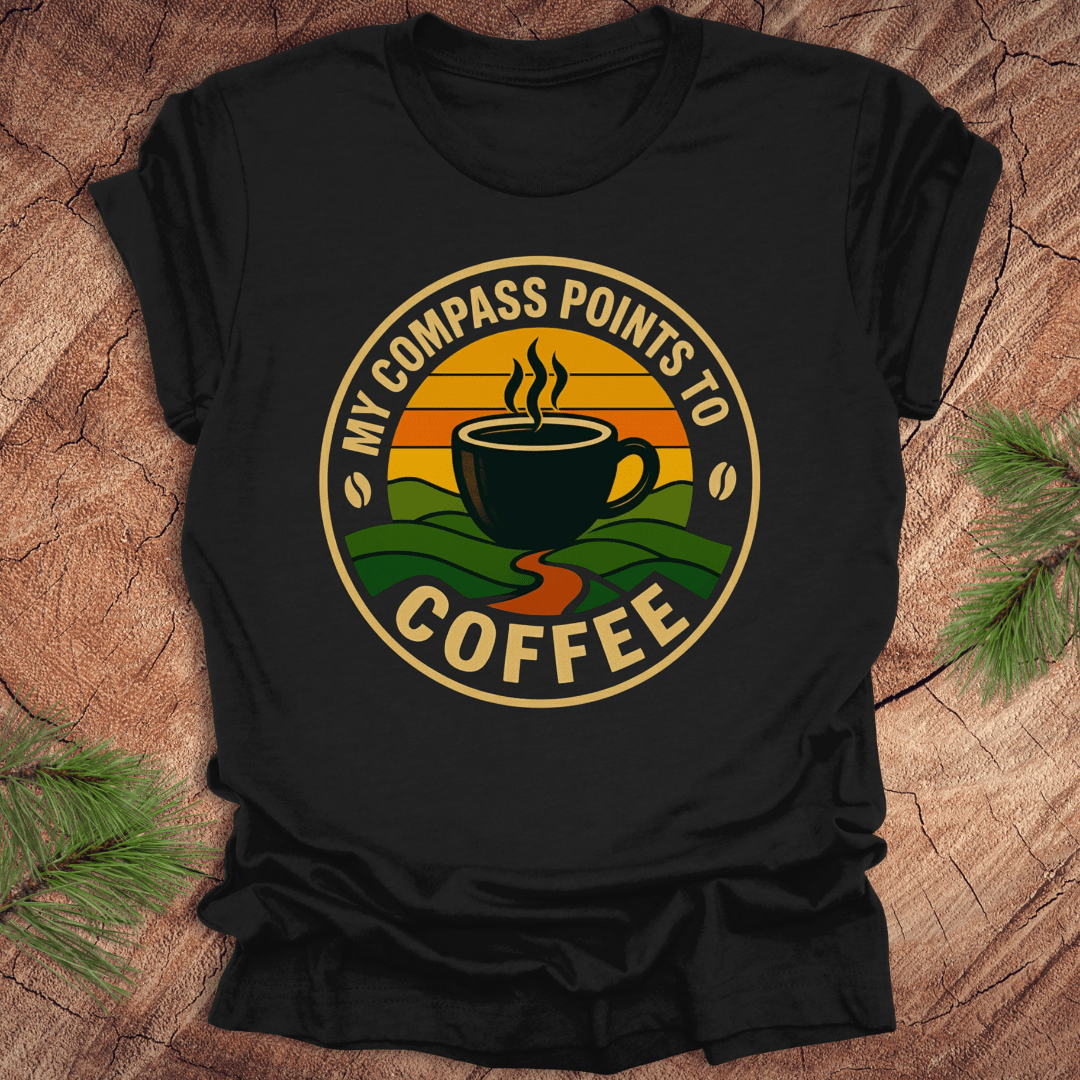 Black t-shirt with a coffee-themed graphic and text, 'my compass points to coffee' on a wooden surface