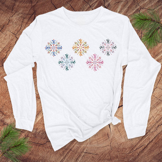 White long-sleeve shirt with colorful folk art snowflake designs on a wooden surface