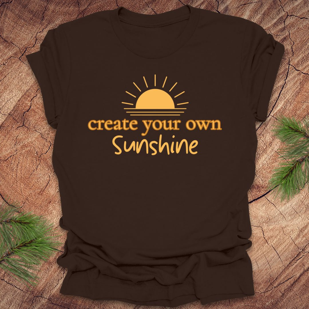 Brown t-shirt with 'create your own sunshine' text and sun graphic on a wooden surface.